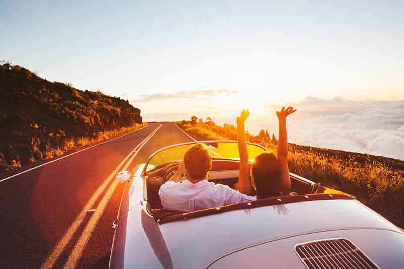 Coppia felice che guida su una strada di campagna verso il tramonto a bordo di un'auto sportiva d'epoca