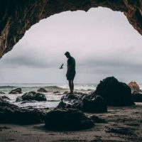 foto de un hombre de pie sobre una roca cerca de la orilla del mar