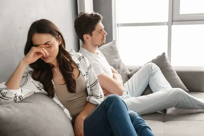 Photo of disappointed couple sitting together on sofa at home with upset look and expressing quarrel isolated over white background