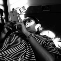 fotografia a preto e branco de uma mulher a escrever no telemóvel enquanto está deitada na cama