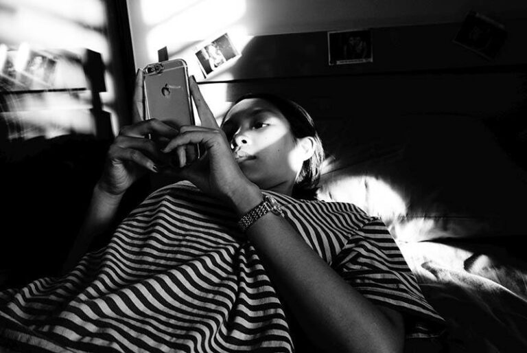 foto in bianco e nero di una donna che scrive sul suo telefono mentre è sdraiata sul letto
