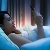 side view of woman lying on bed and typing on phone during night