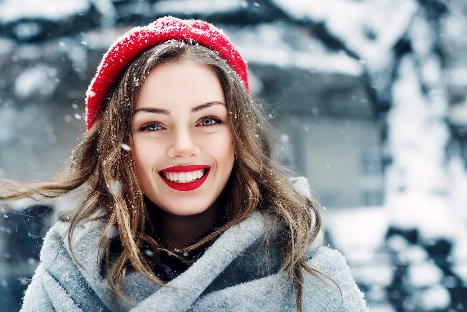 a beautiful smiling brunette with a red cap on her head is standing outside in the snow