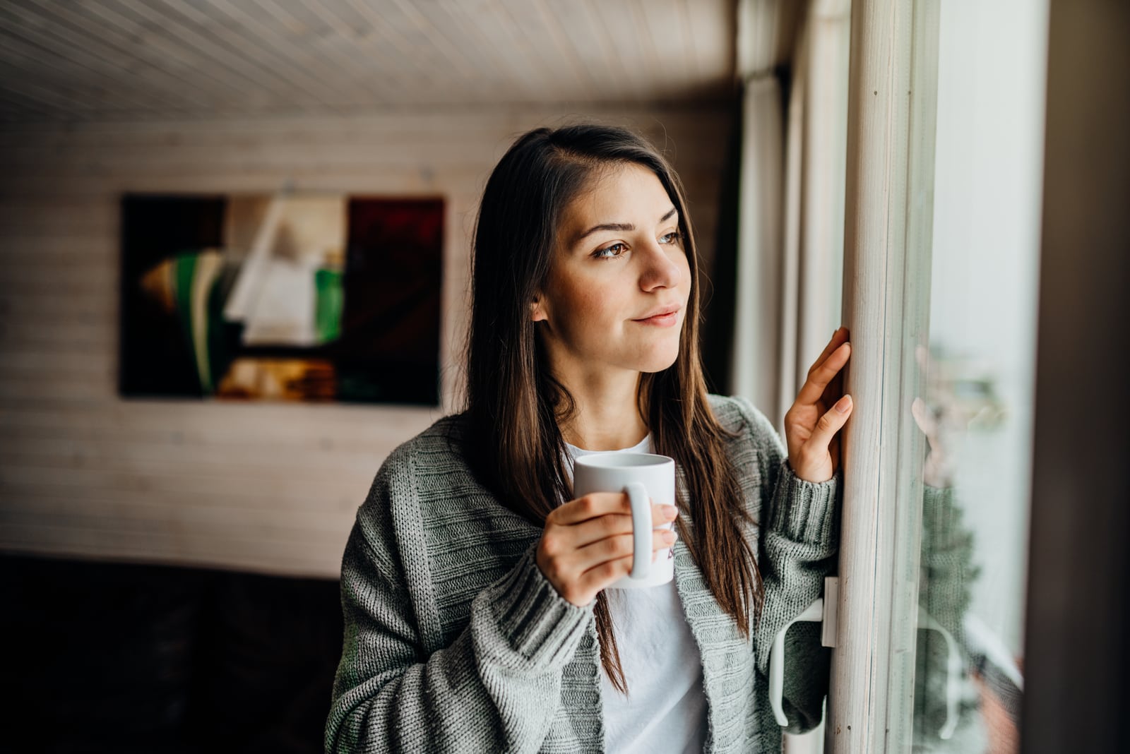 a contented smiling brunette drinks tea and looks out the window