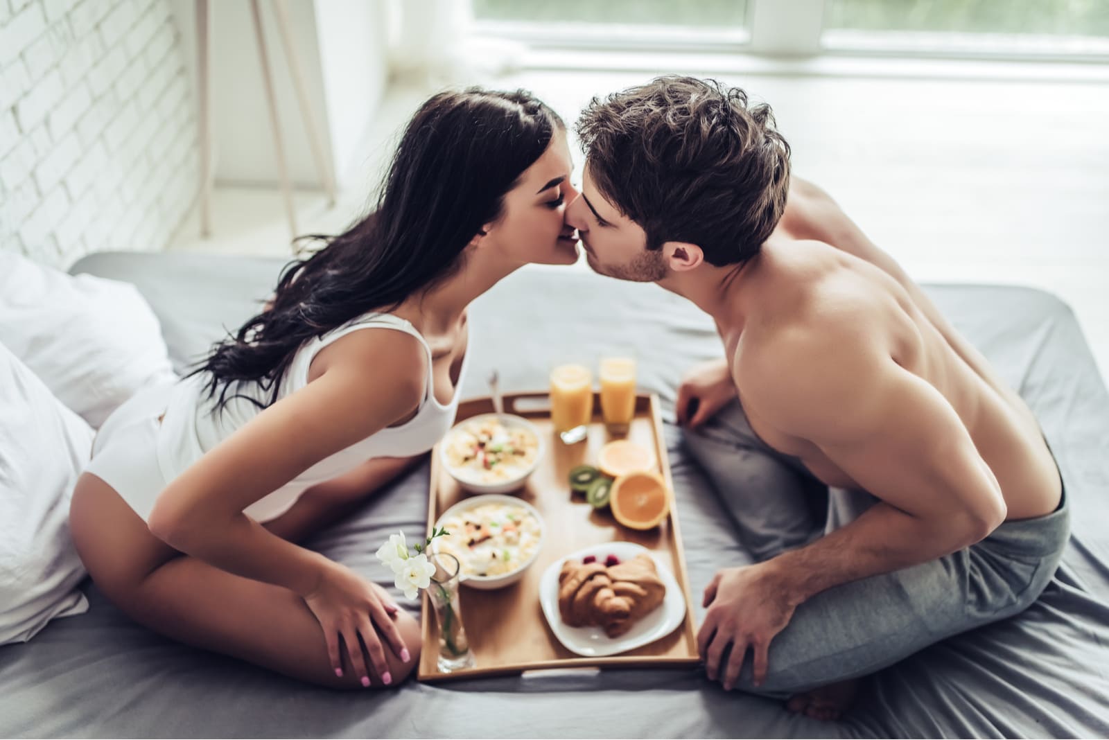 a loving couple kissing on the bed with breakfast.