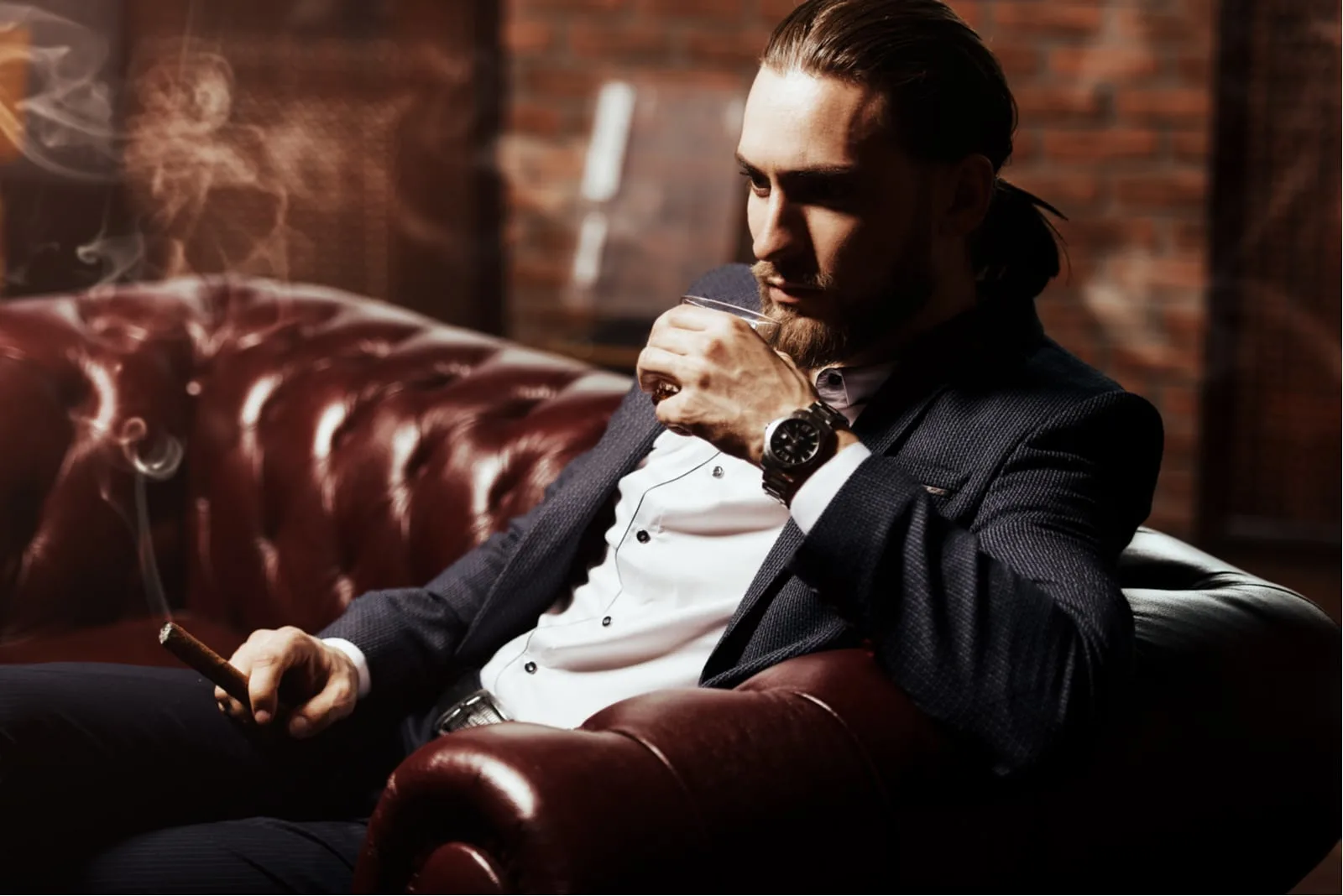 a man sits smoking a cigar and drinking wine