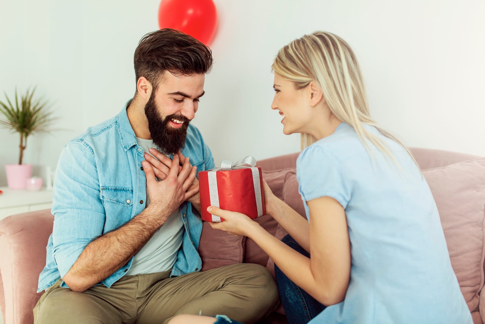 una rubia sonriente entrega un regalo a un hombre sorprendido