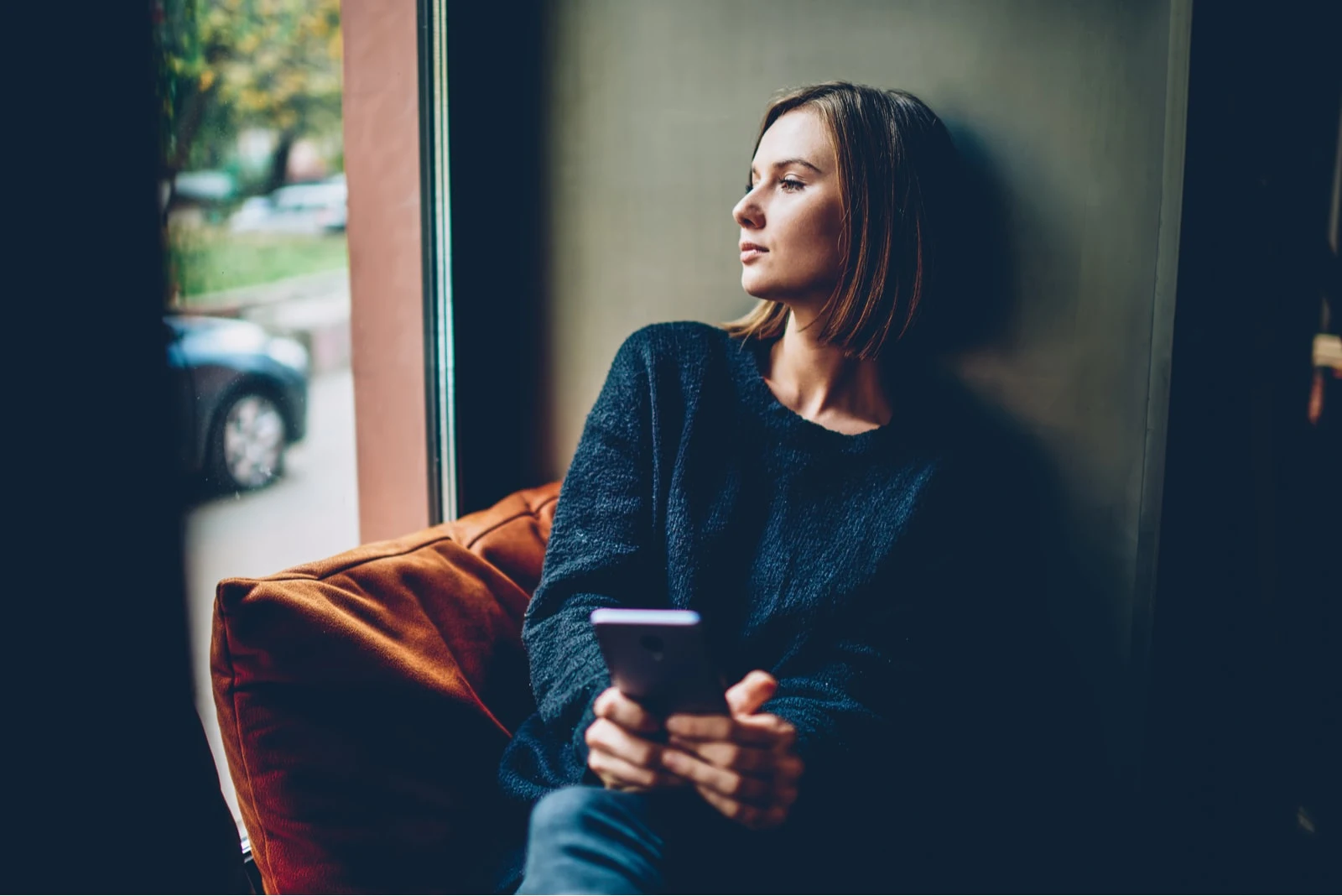 a woman with a phone in her hand is sitting by the window