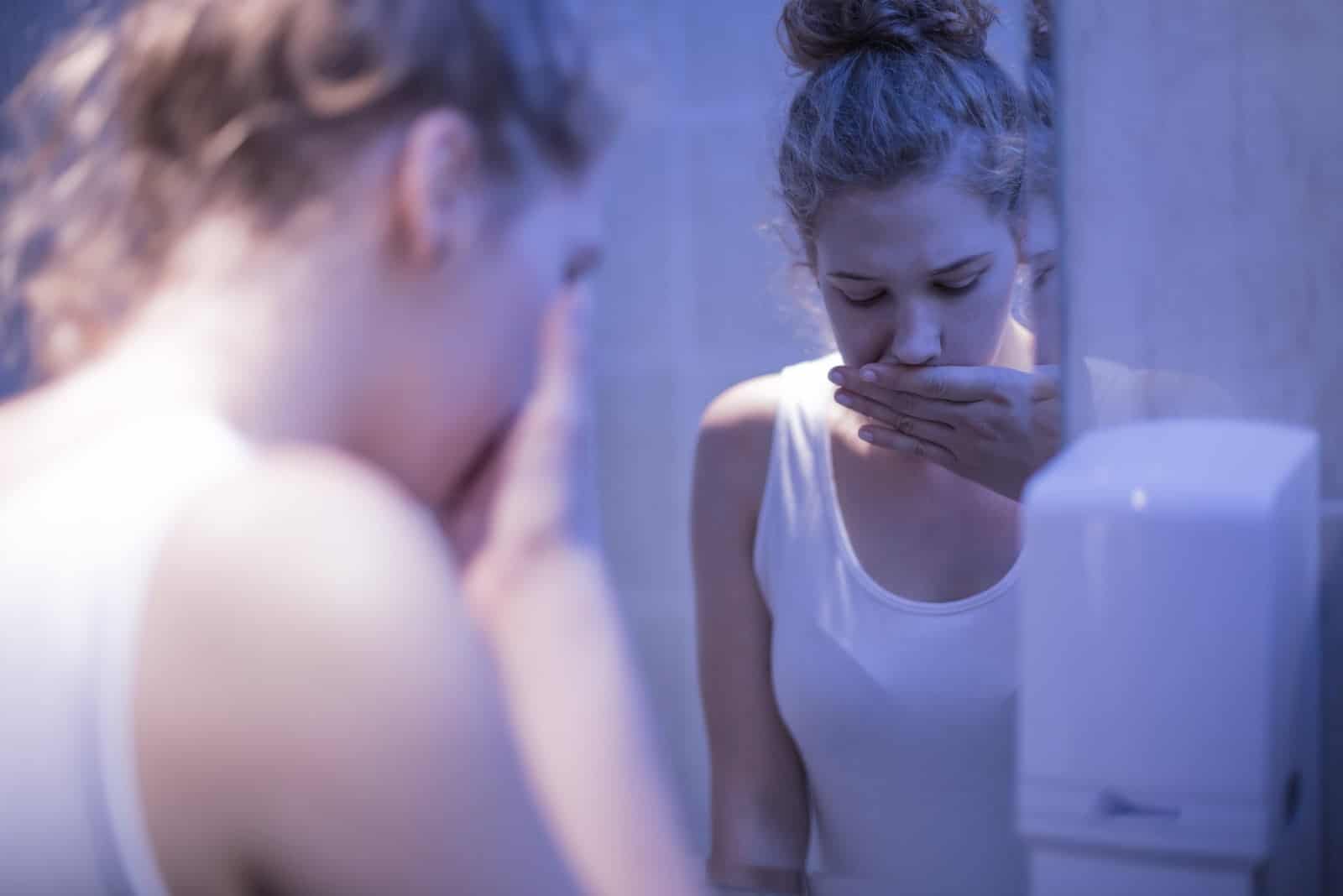 una ragazza malata e preoccupata in piedi davanti a uno specchio