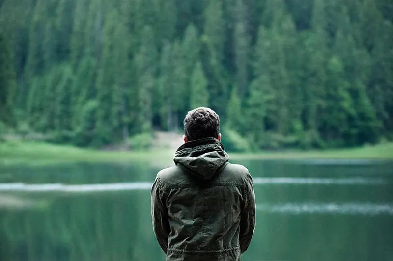 back view of man in jacket standing in front of water