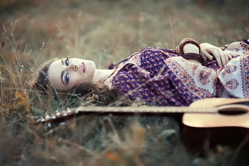 beautiful woman laying on the grass with her guitar