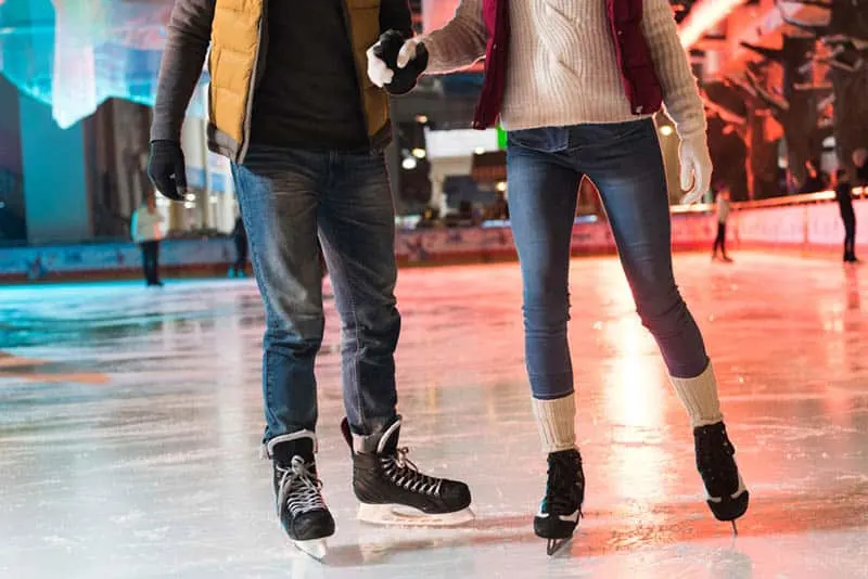 couple in skates holding hands and ice skating on rink