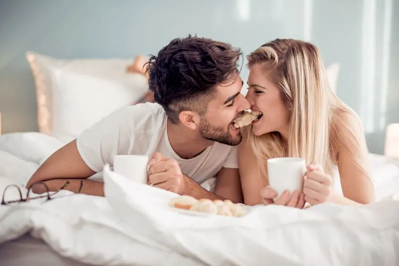 cute couple biting a croissant together on bed