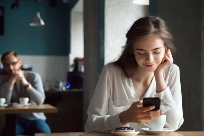 guy with interest looking smiling woman in cafe using phone