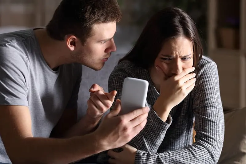 jealous man showing phone to sad woman