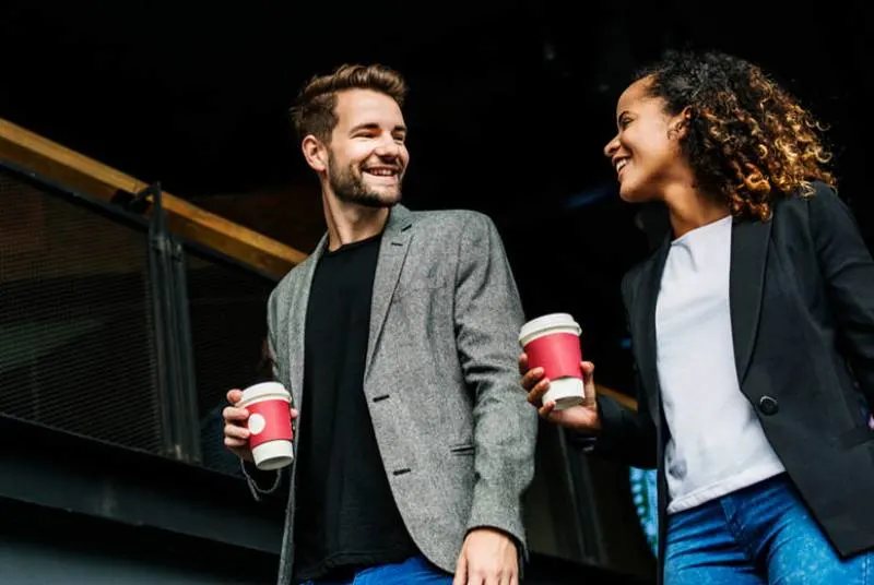 male and female holds cups while walking and looking each other