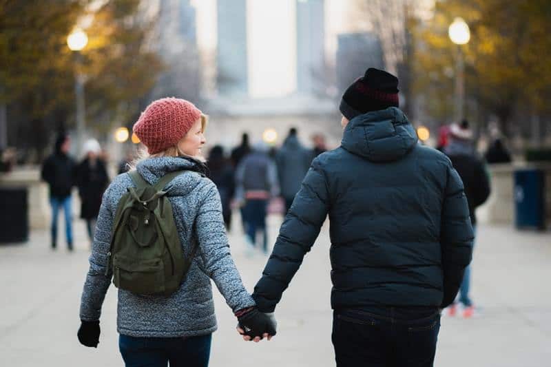 man and woman holding their hands while walking in public