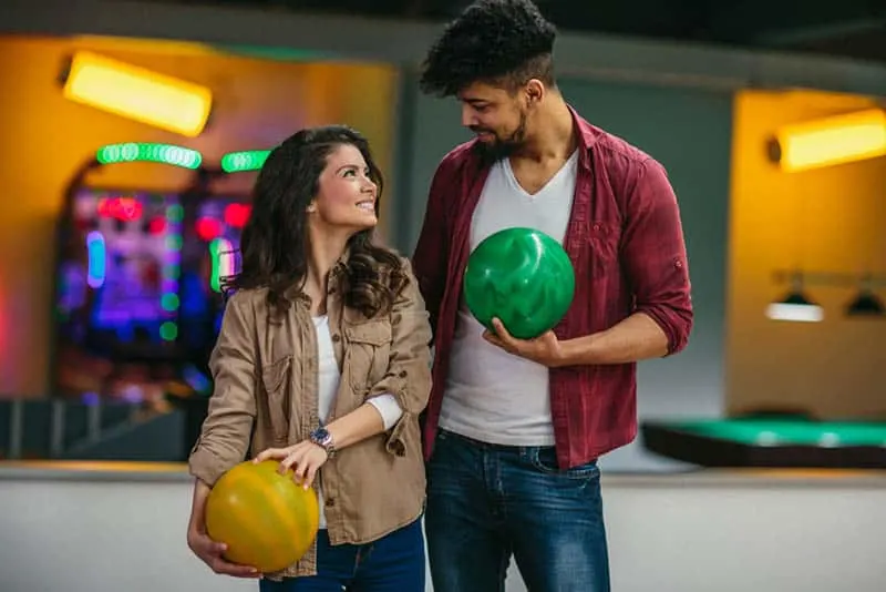 man and woman looking each other and holding bowling ball