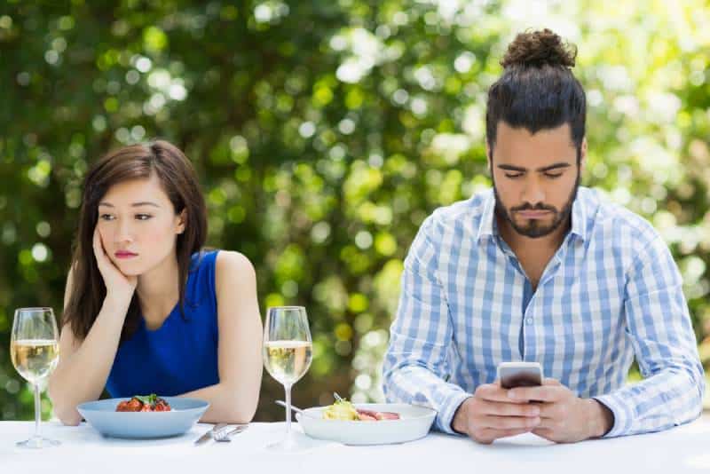man ignoring his girlfriend and using phone