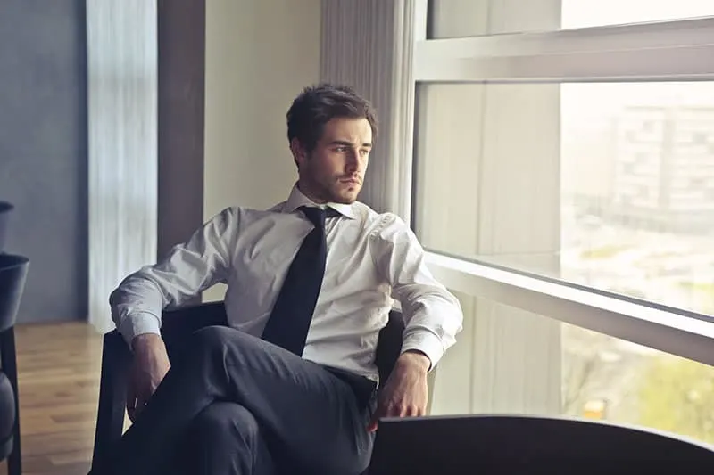man in shirt and tie sitting beside window