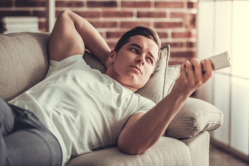 man lying on the couch and watching the television