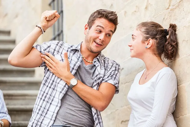 man talking to woman and showing his muscles