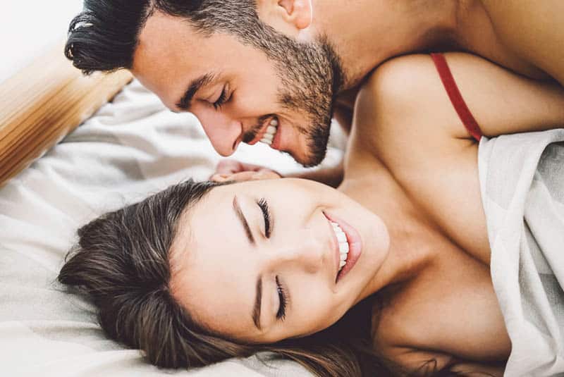 man talking to woman ear in bed