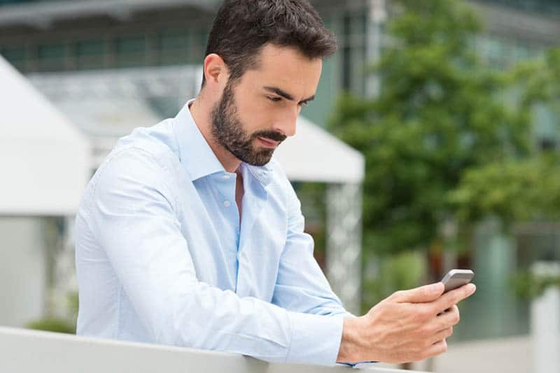 man wearing white shirt standing outside and typing on his phone