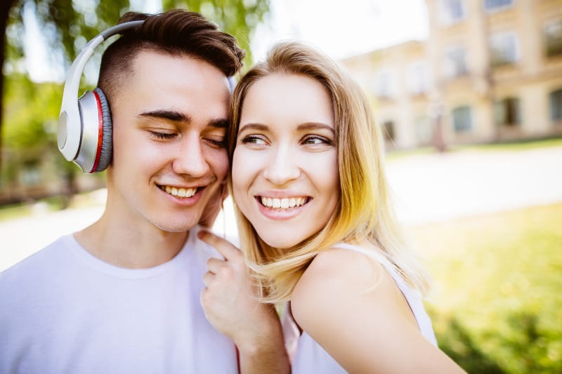 man with headset listening to music while woman leaning on headset