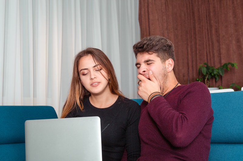 man yawning while looking at laptop beside woman at home