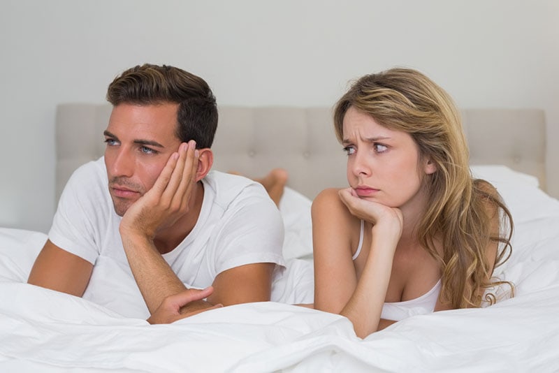 sad woman looking at serious man on the bed