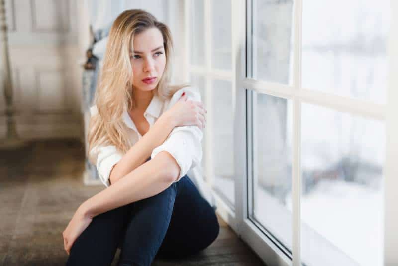 sad woman sitting on parquet floor by window