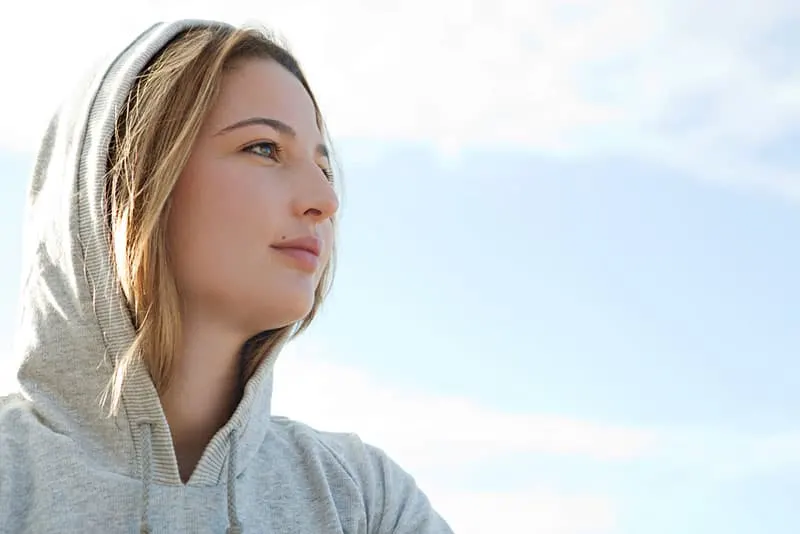 Close up portrait of a beautiful young sports woman wearing a hood during a sunny morning against a blue sky