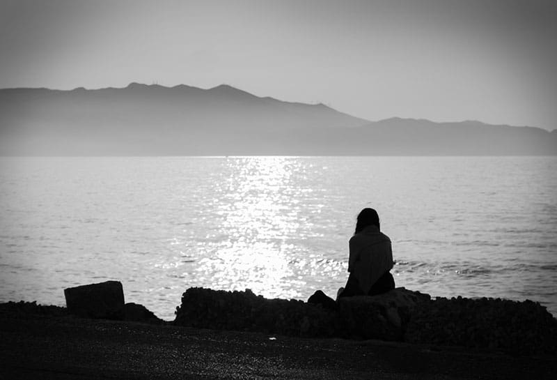 depression. black and white photo of a melancholic girl sitting alone by the sea feeling sad and contemplating