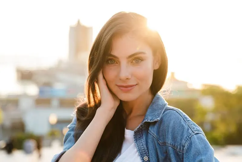 Portrait of a beautiful smiling young brunette woman standing outdoors with cityscape background, posing