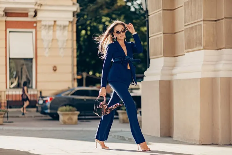 luxury rich woman dressed in elegant stylish blue suit walking in city on sunny autumn day holding purse, fashion trend 
