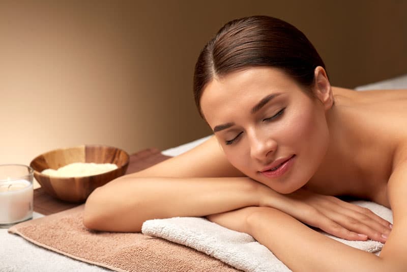 wellness, beauty and relaxation concept - young woman lying at spa or massage parlor