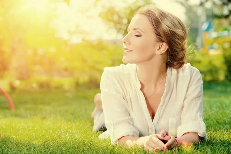 Beautiful smiling woman lying on a grass outdoor. She is absolutely happy.