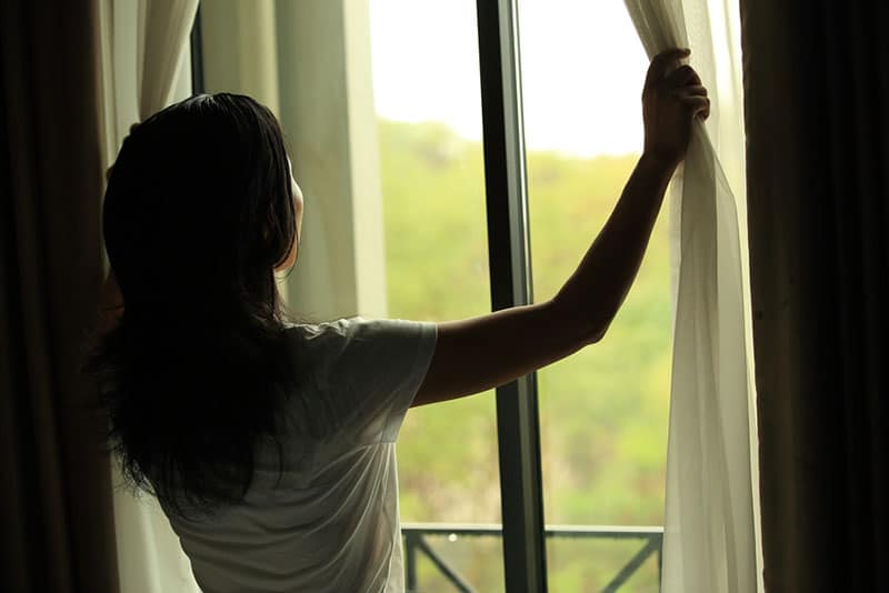 young woman opening curtains in a bedroom
