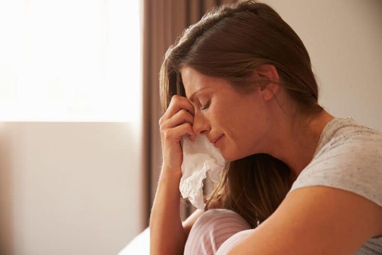 Donna affetta da depressione seduta sul letto e piangente