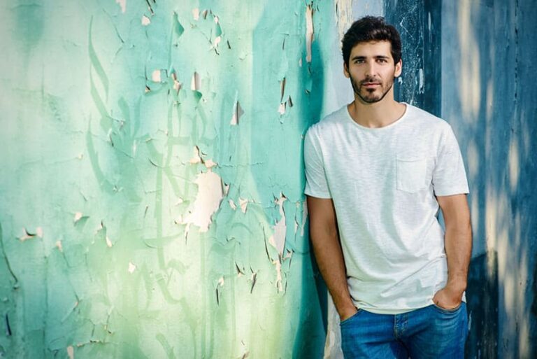 Portrait of a handsome young man in jeans and white t-shirt leaning to the old wall.