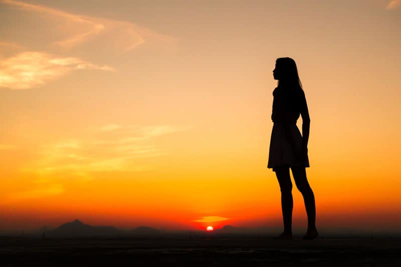 Silhouette of free woman enjoying freedom feeling happy at sunset. Serene relaxing woman in pure happiness 