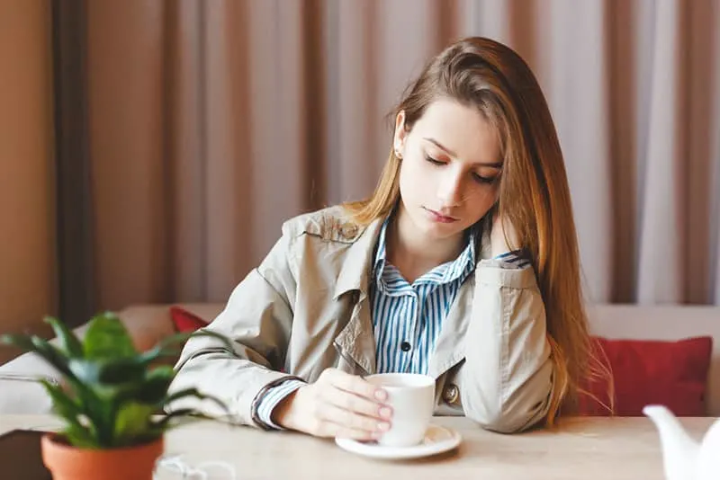 Unemployed woman sits alone heartbroken at coffee shop dwelling in sadness about her lack of career