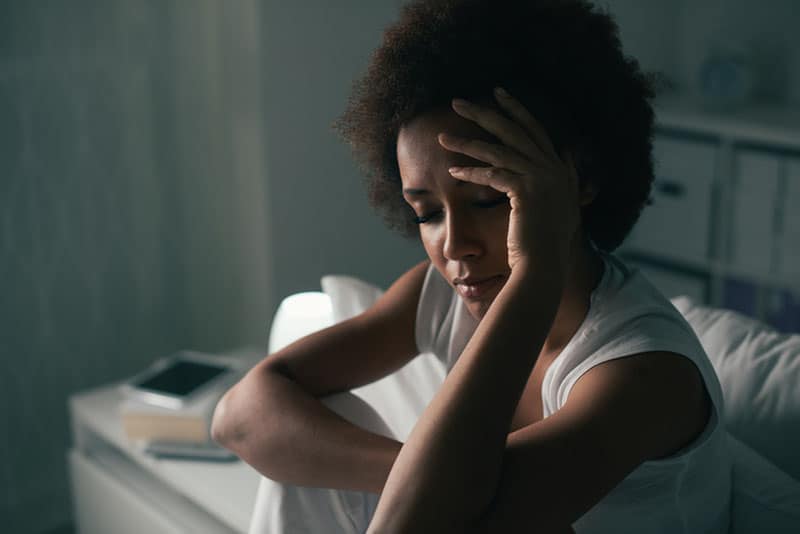 Triste donna depressa che soffre di insonnia, è seduta a letto e si tocca la fronte, disturbo del sonno e concetto di stress