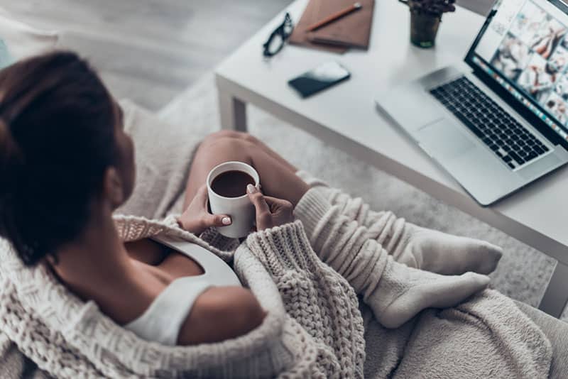 Disfrutando de un café recién hecho. Vista superior de hermosa mujer joven sosteniendo la taza mientras se relaja en el sofá en casa. 