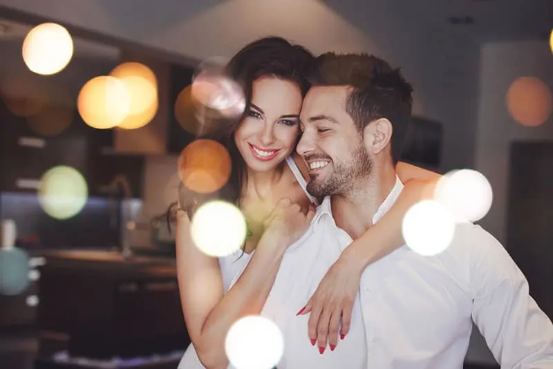 Young successful couple smiling, woman embrace man indoors, bokeh