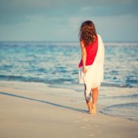 Mujer joven atractiva que camina a lo largo de la playa del océano en la puesta del sol