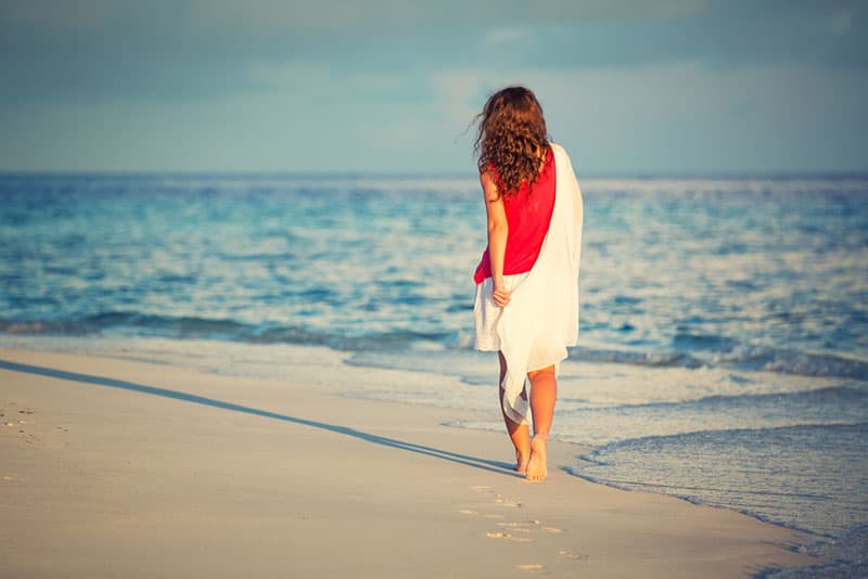Attractive young woman walking along ocean beach at sunset