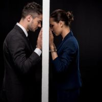 Side view of sad couple in formal wear separated by wall isolated on black