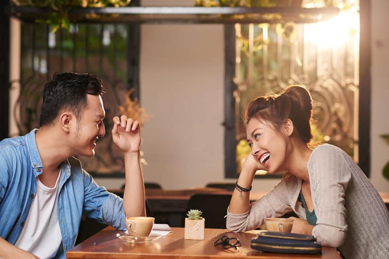 Retrato de lado de una pareja asiática riendo disfrutando de una cita en un café